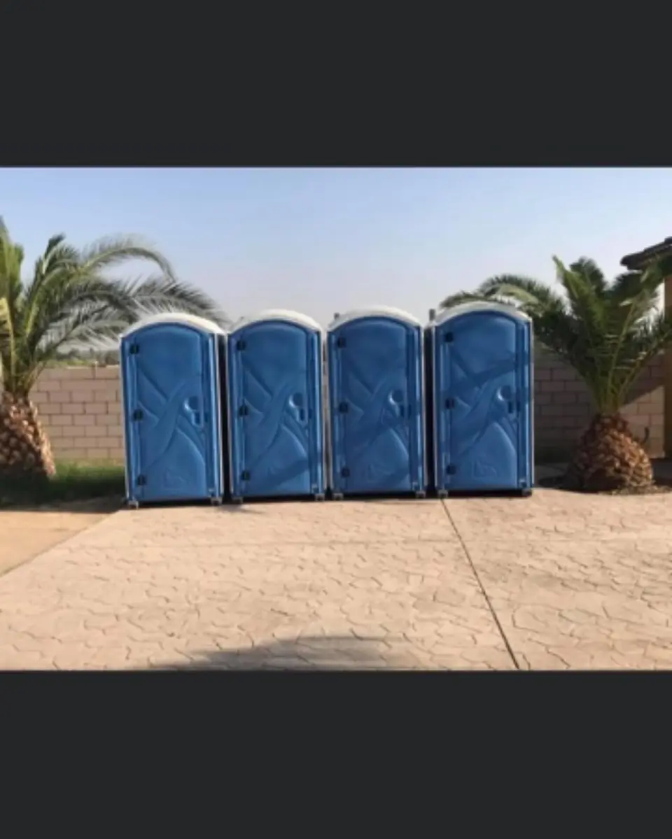 Row of four blue porta potties lined up on pavement for an event
