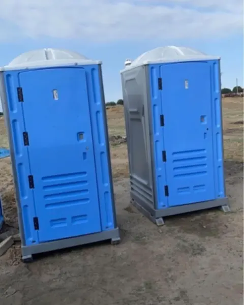 Two blue standard porta potties set on a dirt lot at a construction site