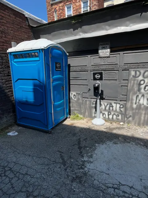 Blue standard porta potty placed on an alley pad behind a building